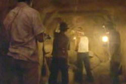 Four men holding lanterns as they walk down a mining tunnel.
