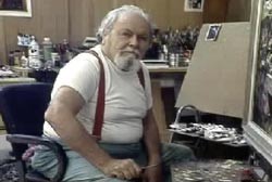 Ben Stahl sitting in front of a painting, wearing a white shirt and red spenders, facing the camera.