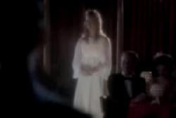 A woman in a bright white dress standing in the middle of a dining room. There is a man in a tuxedo sitting at a table near her.