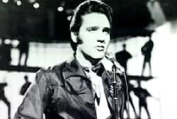Elvis Presley performing on a stage with backup dancers on scaffolding