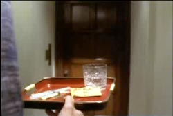 A man holding a tray with a glass of water and pills on it as he approaches a door.