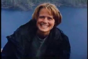 A young woman, Amy Bechtel, in a parka posing infront of a lake.