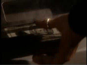 A hand with a gold ring on the thumb is reaching for a stack of money.
