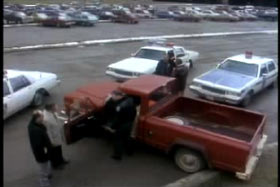 A red pick up truck surrounded by police officers and three patrol cars.