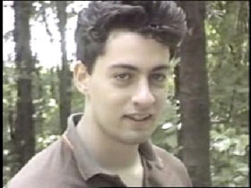James Kimball, a young man with short brown hair and a brown collar shirt in front of a row of trees.