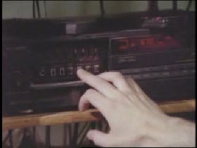 A hand presses a button on stereo.