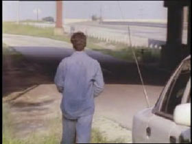A man in a denim shirt and jeans walking down an empty road.