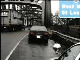 A black sedan abandoned on the shoulder of the road right before a bridge.