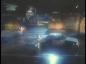 A woman holding a baby and walking towards a white sedan in a deserted junkyard.