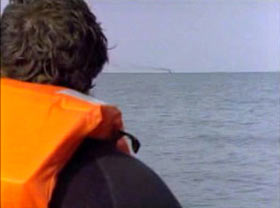 A man in an orange life vest looks out over the water.