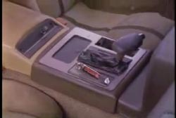 A close up on the center console on a car, showing the gear shift and a can of mace next to it.