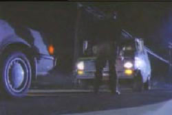 A man standing inbetween two car that are stopped on a street at night.