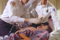 Two paramedics stand over a man and try to put an oxygen mask over his mouth and nose.
