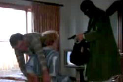 Roger ties up his wife with a rope as a gunman in a ski mask points his firearm at him