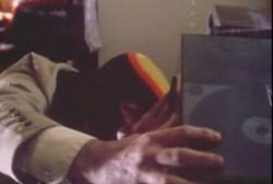 Man with a ski mask on looking under objects in a room