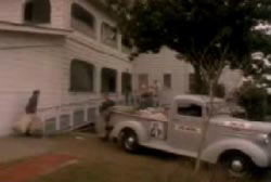 People carrying white sacks of letters into a house from the bed of a pick up truck