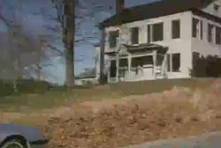 Georgia driving up the road with a large 2 story white and brown house