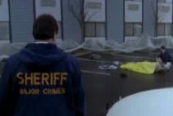 Police sheriff walking up to the scene of the crime where an officer is covering Blair's body