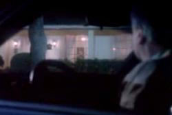 A man watches the house at night from his car