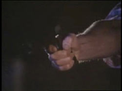 arm extended from the shadows aiming a pistol at someone