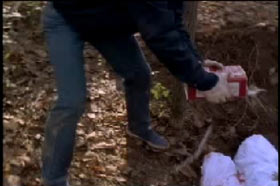 Bishop pouring gasoline onto covered bodies in a shallow grave in the woods
